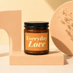 Amber glass candle with black lid on a peach-colored block, labeled "Everyday Love."