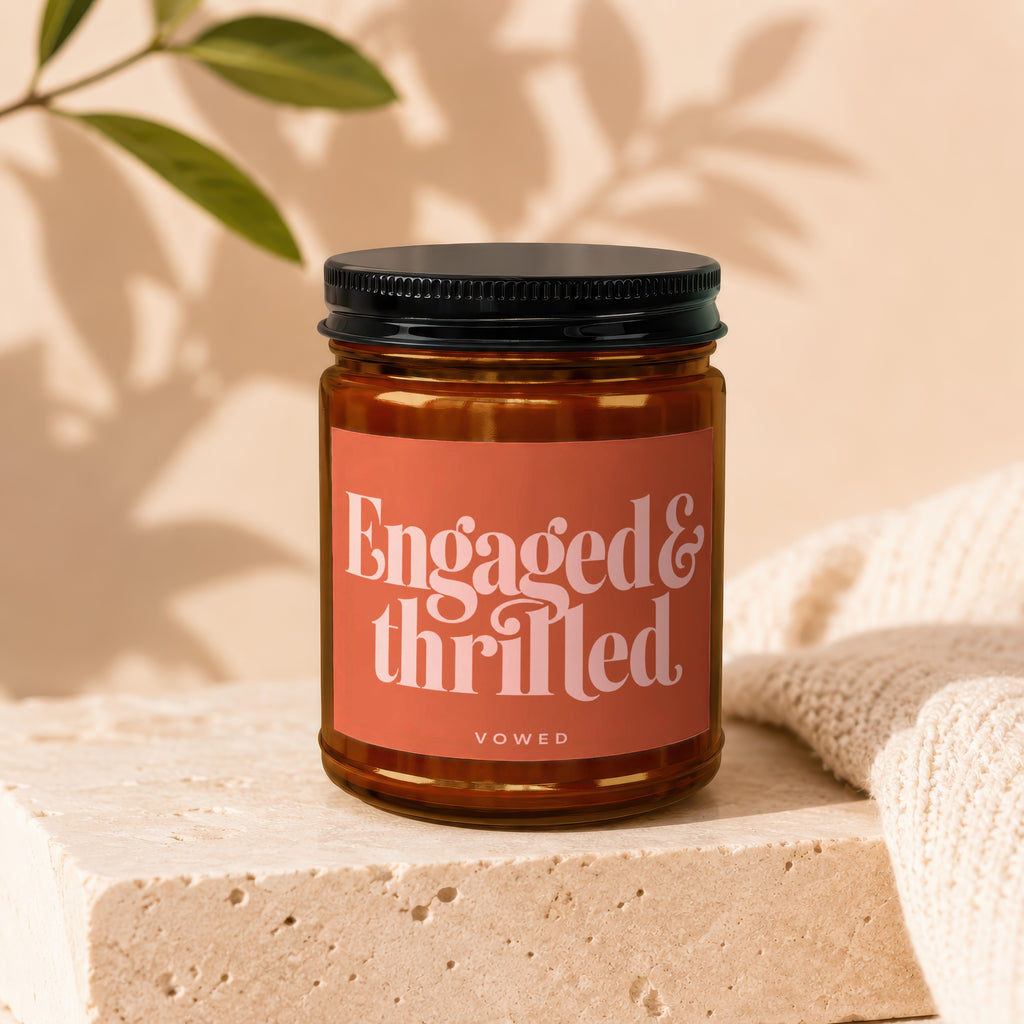 Amber candle in a jar with a black lid, labeled "Engaged & thrilled" and "vowed."
