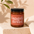 Amber candle in a jar with a black lid, labeled "Engaged & thrilled" and "vowed."