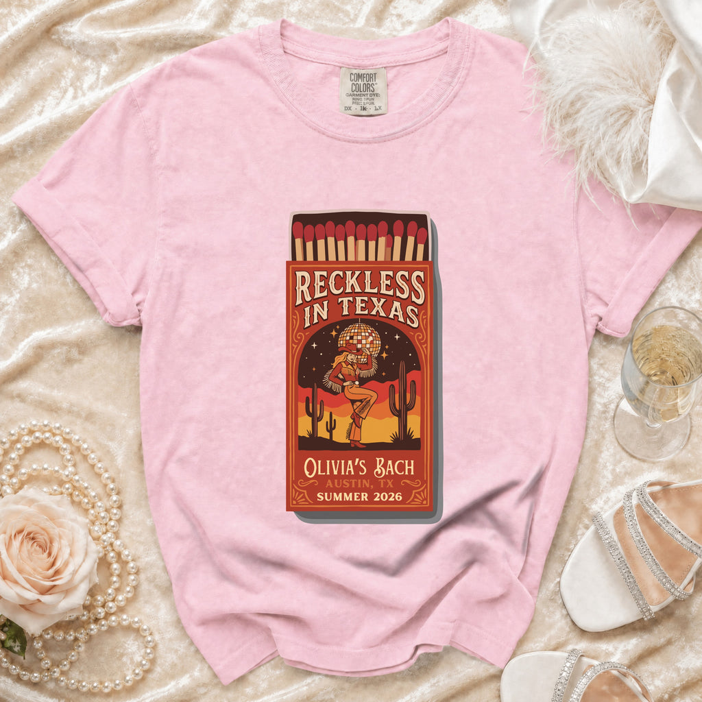 Pink t-shirt with "Reckless in Texas" matchbox graphic and event details.