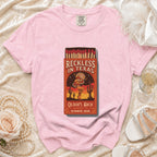 Pink t-shirt with "Reckless in Texas" matchbox graphic and event details.