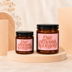 Two amber glass candles with black lids, pink labels reading "Our officiant is a legend."