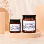 Two amber glass candles on peach pedestals with black lids, labeled "Forever Bewitched."