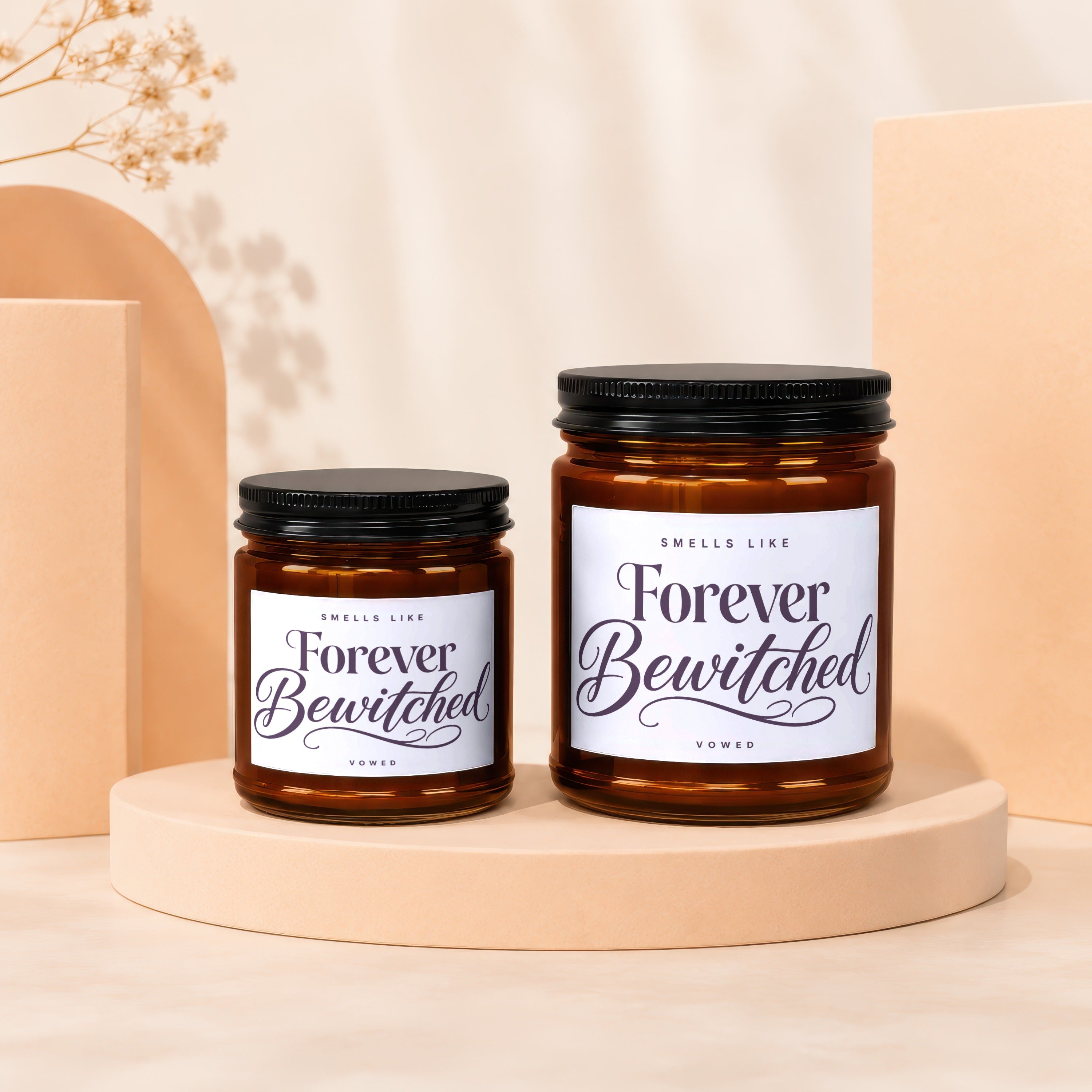 Two amber glass candles on peach pedestals with black lids, labeled "Forever Bewitched."