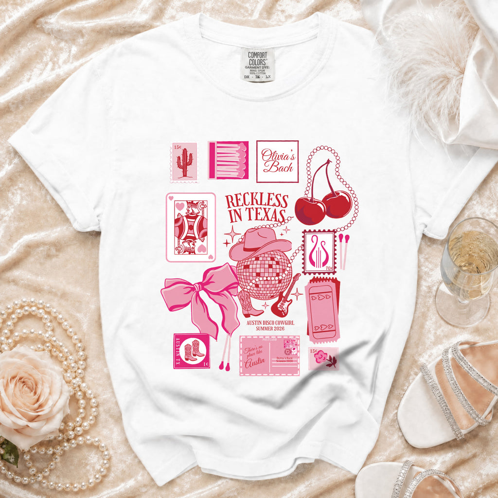 White t-shirt with pink graphics: "Olivia's Bach Reckless in Texas", disco ball, cards.