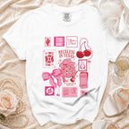 White t-shirt with pink graphics: "Olivia's Bach Reckless in Texas", disco ball, cards.