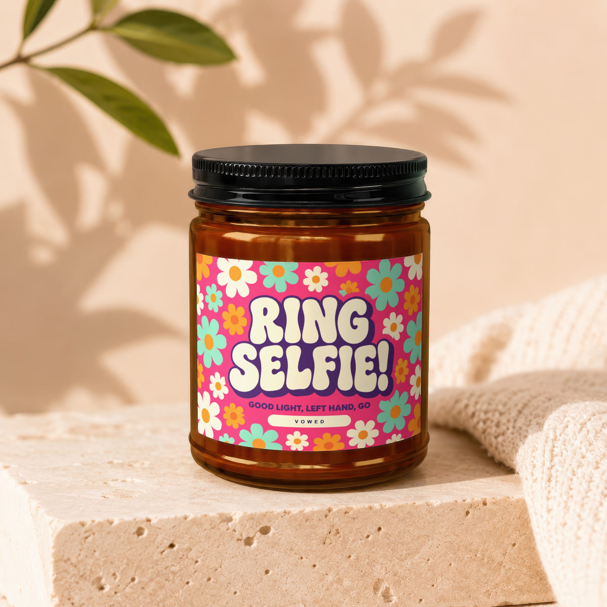 An amber glass jar with a black lid rests on a textured stone surface, featuring a colorful daisy-patterned label with retro text reading "RING SELFIE!".
