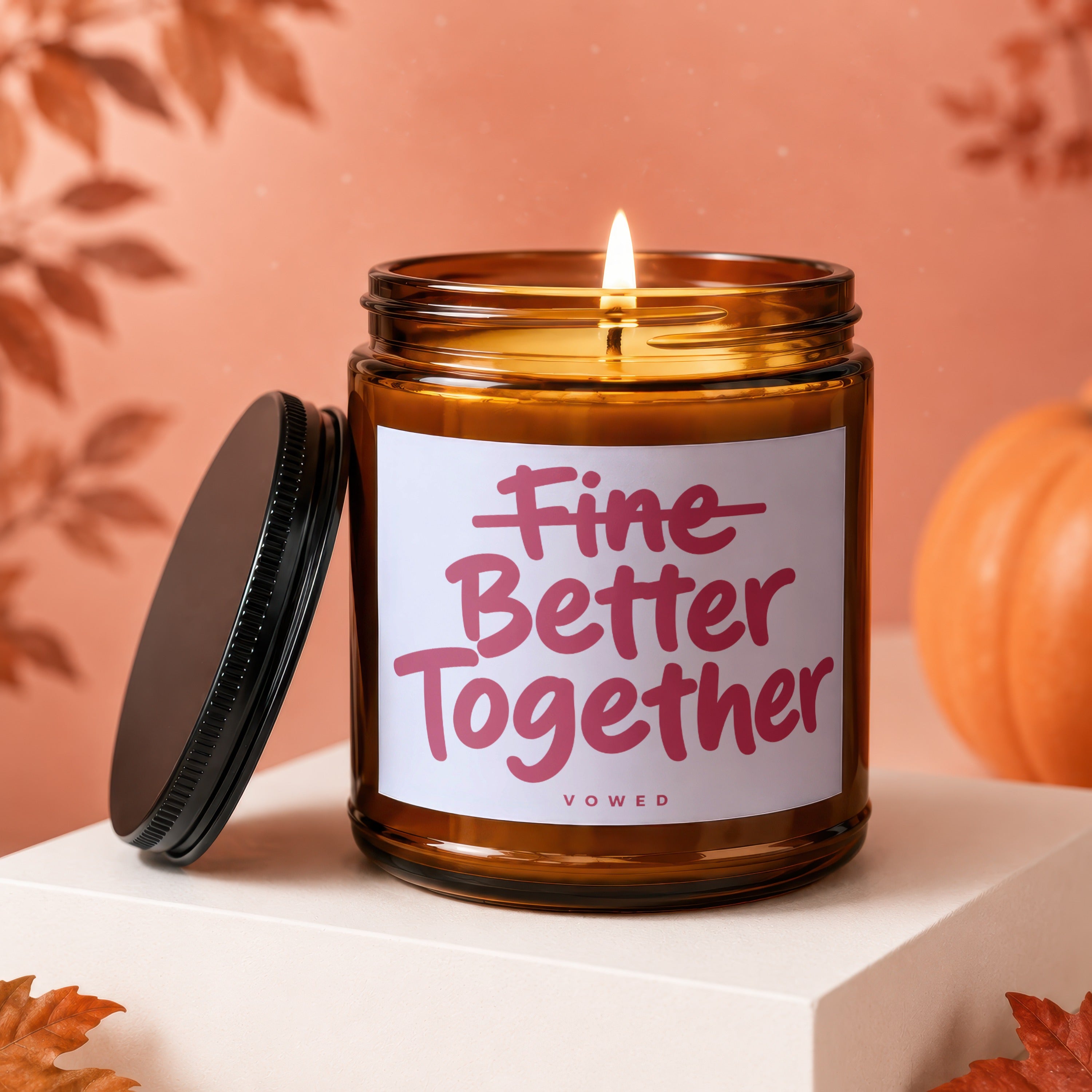 Brown glass candle with lit flame, lid beside it, and text "Fine Better Together".