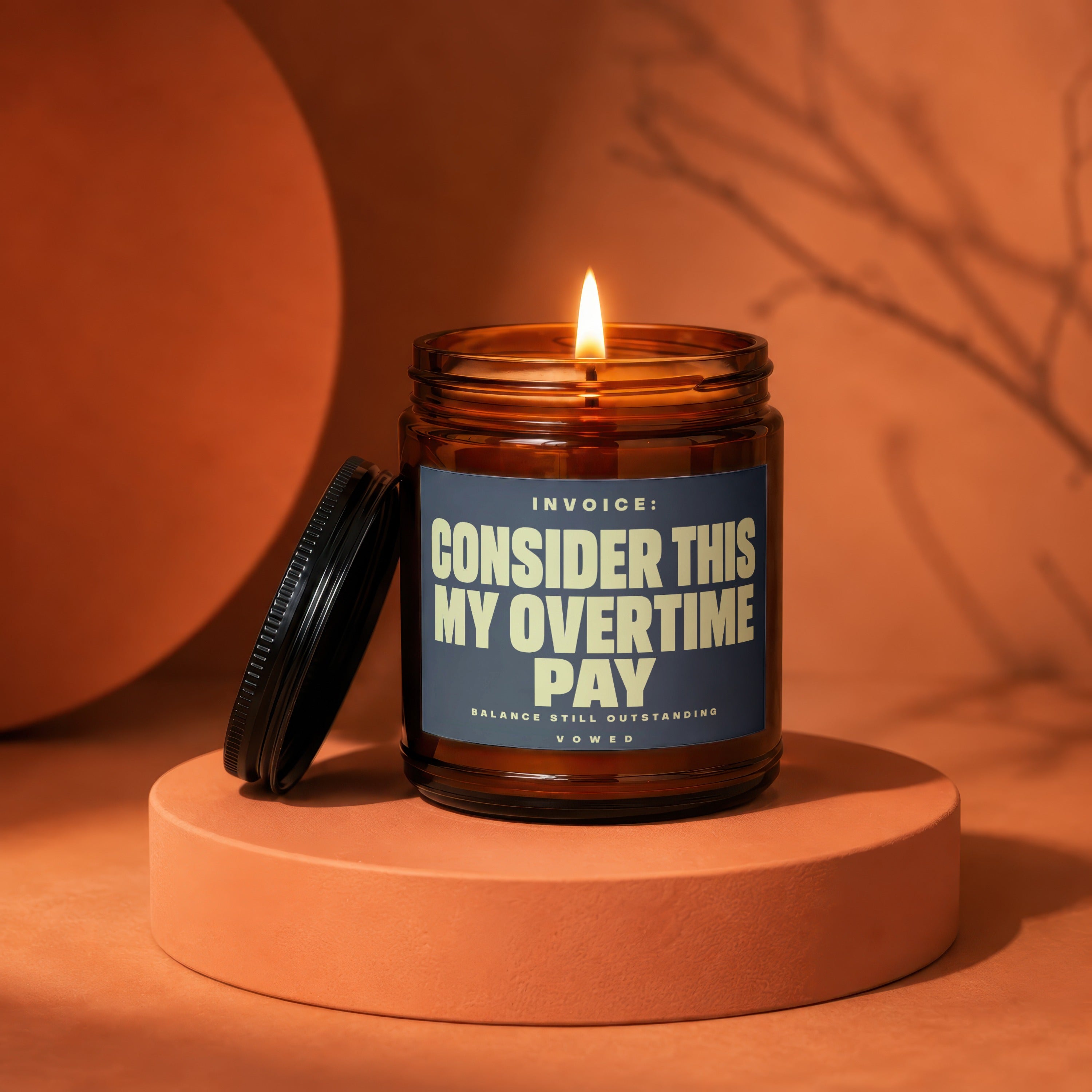 Amber candle with lit flame, label reads "Invoice: Consider This My Overtime Pay".