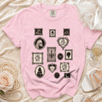 Pink t-shirt with framed gothic-themed prints including a skull, cake, and text.
