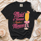 Black t-shirt with "Maid of Honour Needs a Mimosa" text and a mimosa glass graphic.