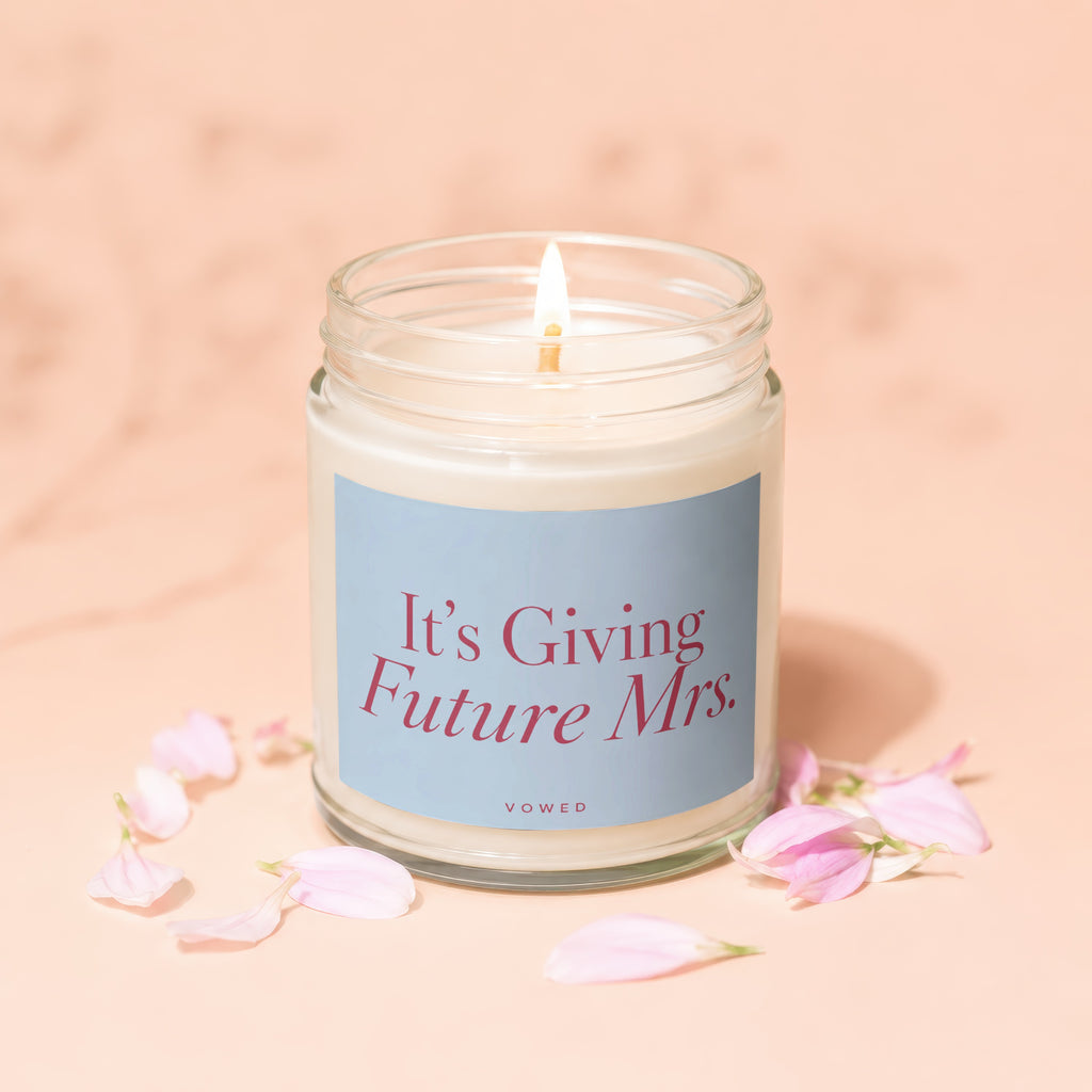 Candle with text "It's Giving Future Mrs." and word "VOWED" above pink petals.