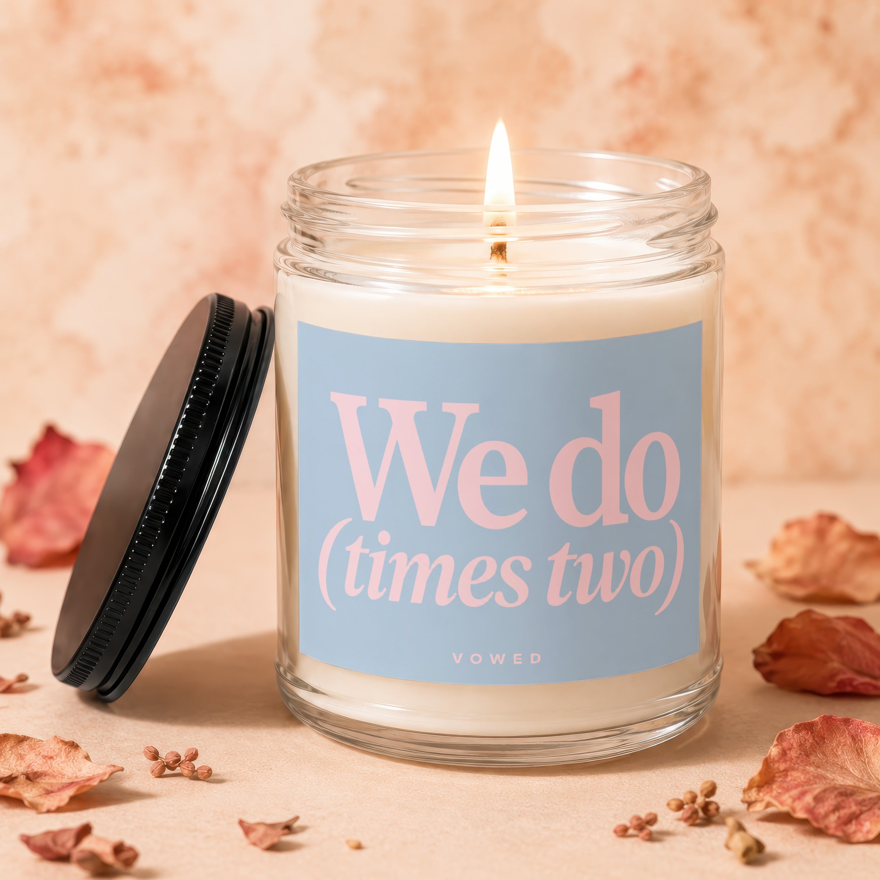 Lit candle in glass jar with blue label reading "We do (times two) VOWED".