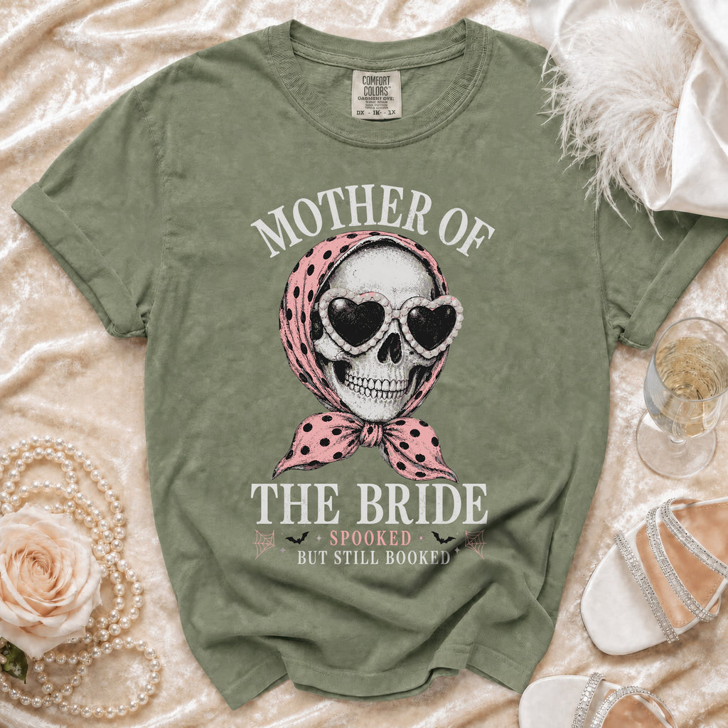 Green t-shirt with skull wearing pink polka dot scarf and heart sunglasses, reading "Mother of the Bride Spooked but Still Booked."