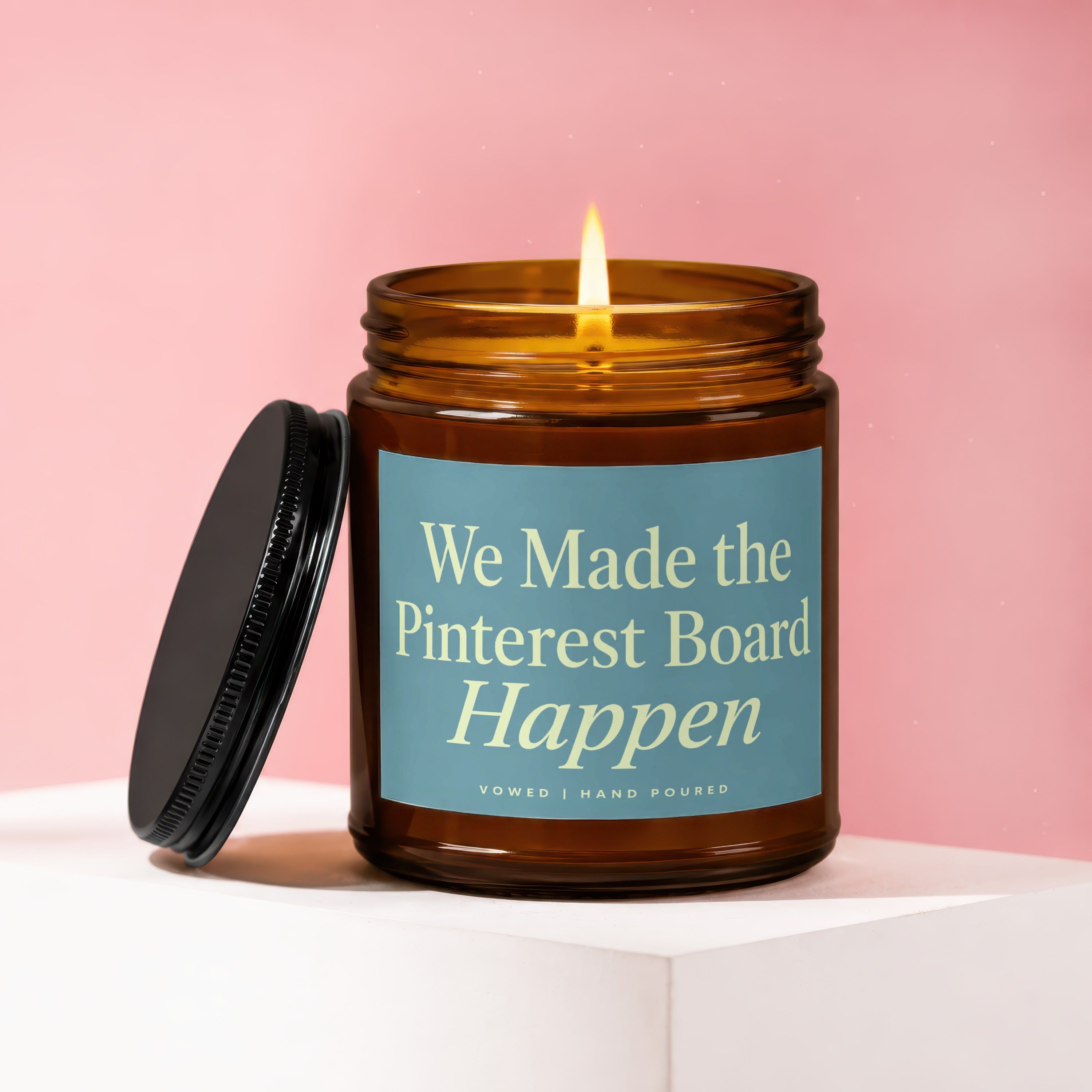 Amber jar candle with lit flame, lid off, features text "We Made the Pinterest Board Happen".