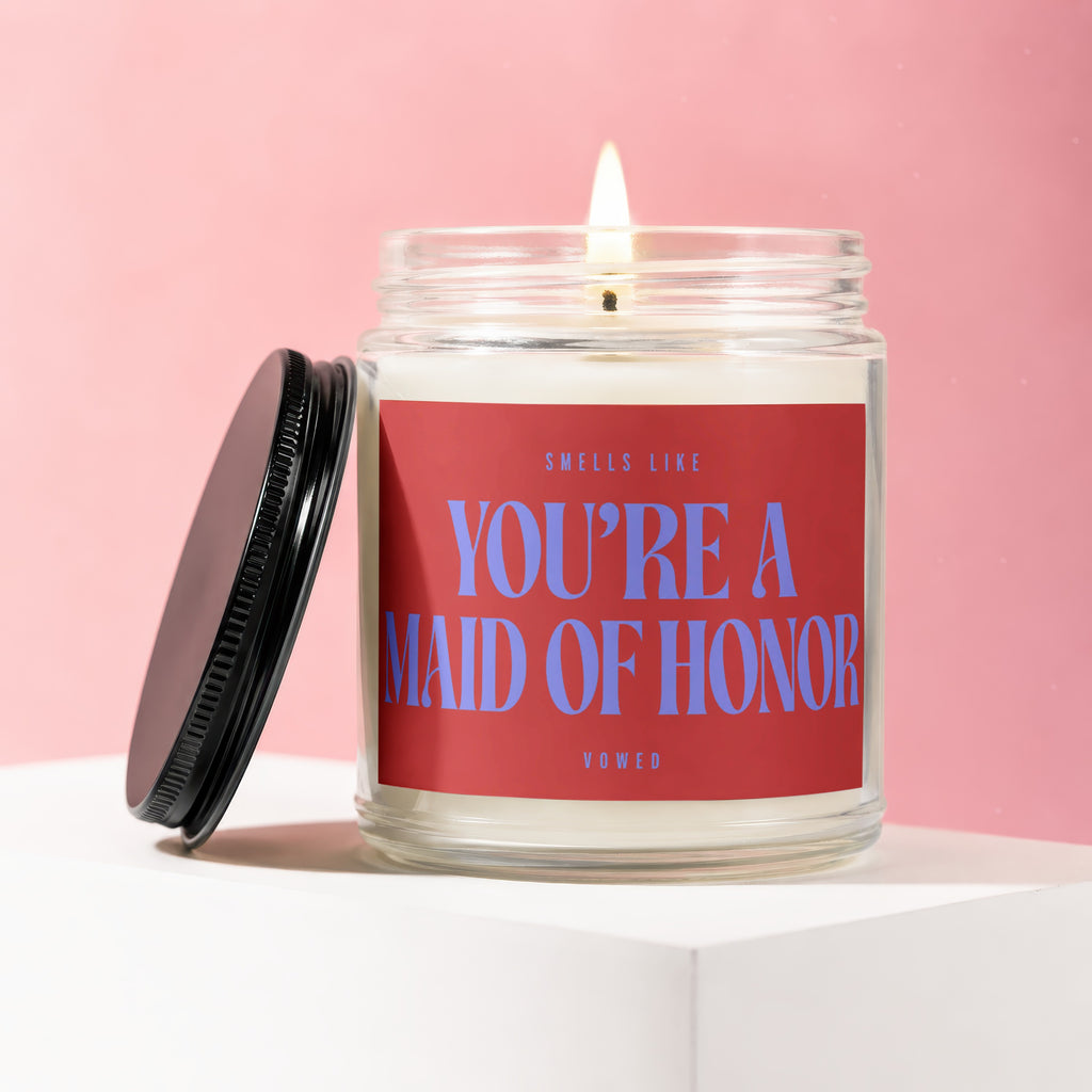 Candle with red label saying "Smells Like You're A Maid of Honor".