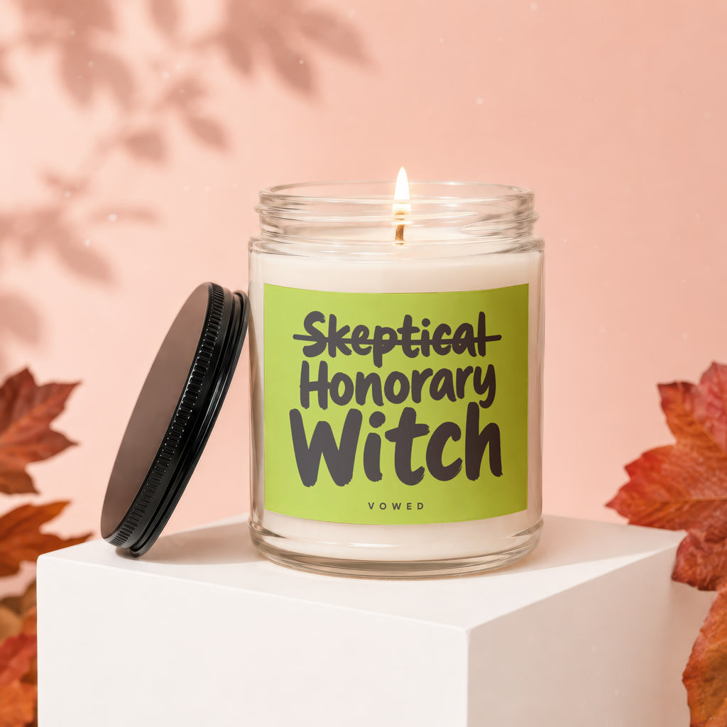 Lit glass candle with a green label that reads "Skeptical Honorary Witch."