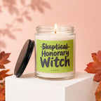 Lit glass candle with a green label that reads "Skeptical Honorary Witch."