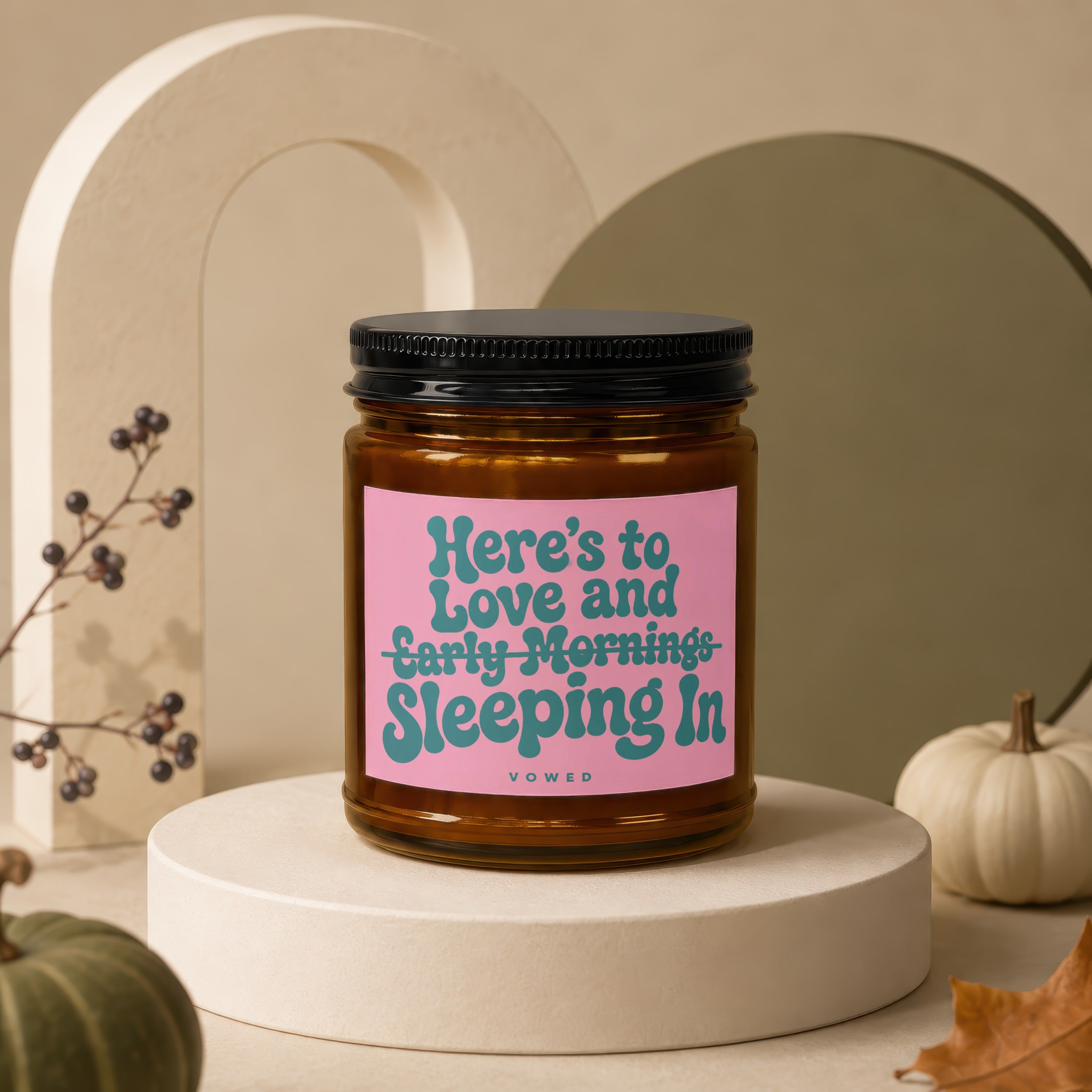 Amber jar candle with pink label reading "Here's to Love and Early Mornings, Sleeping In".
