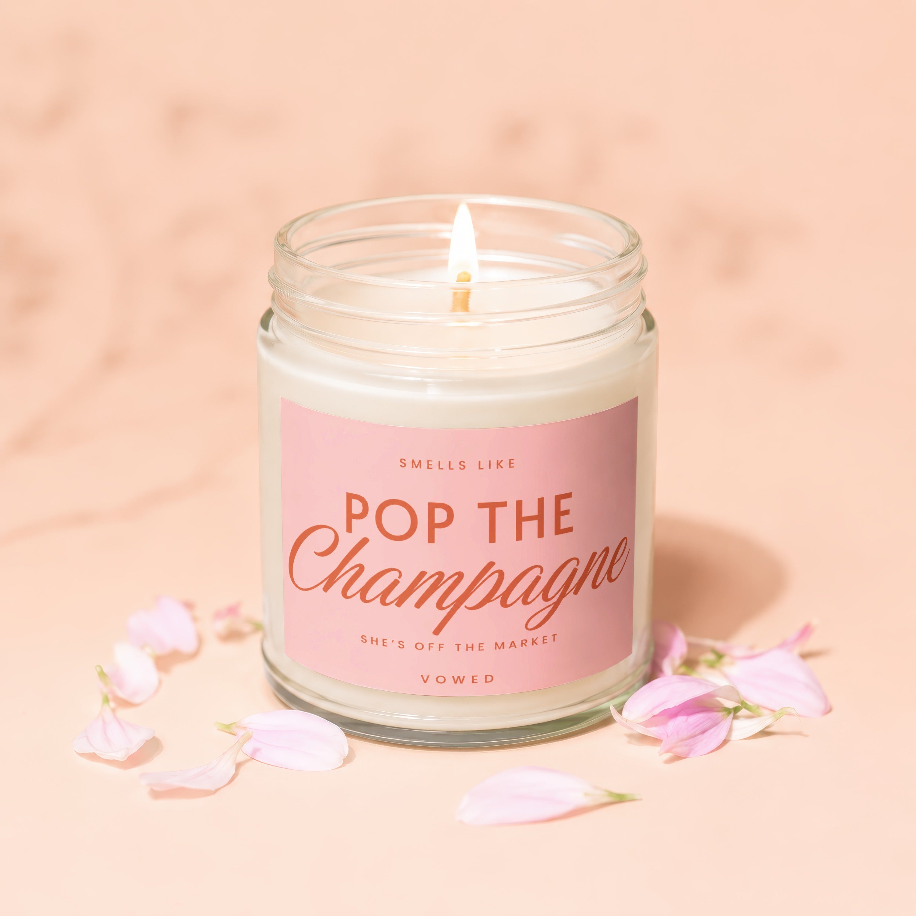 Candle with pink label reads "Smells Like Pop The Champagne She's Off The Market Vowed"