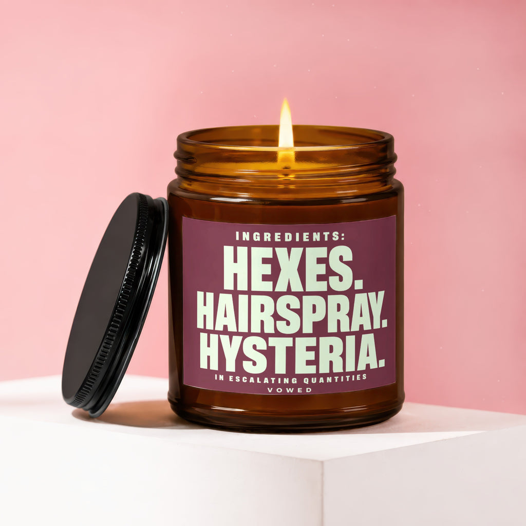 Amber glass candle with a lit wick and maroon label featuring text.