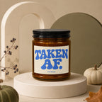 Brown glass candle with black lid, label reads "TAKEN AF. VOWED."
