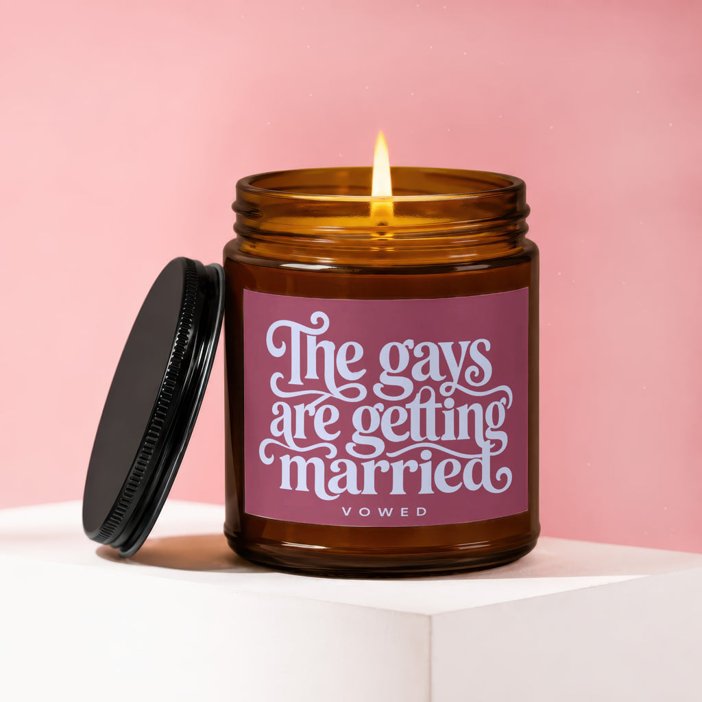 Amber candle with lit flame, black lid askew, reads "The gays are getting married vowed".