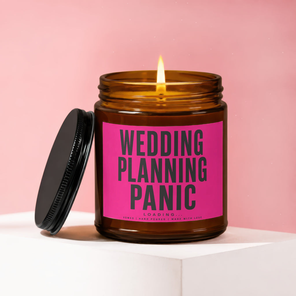 Amber glass candle with lit wick and pink label reading "Wedding Planning Panic Loading..."