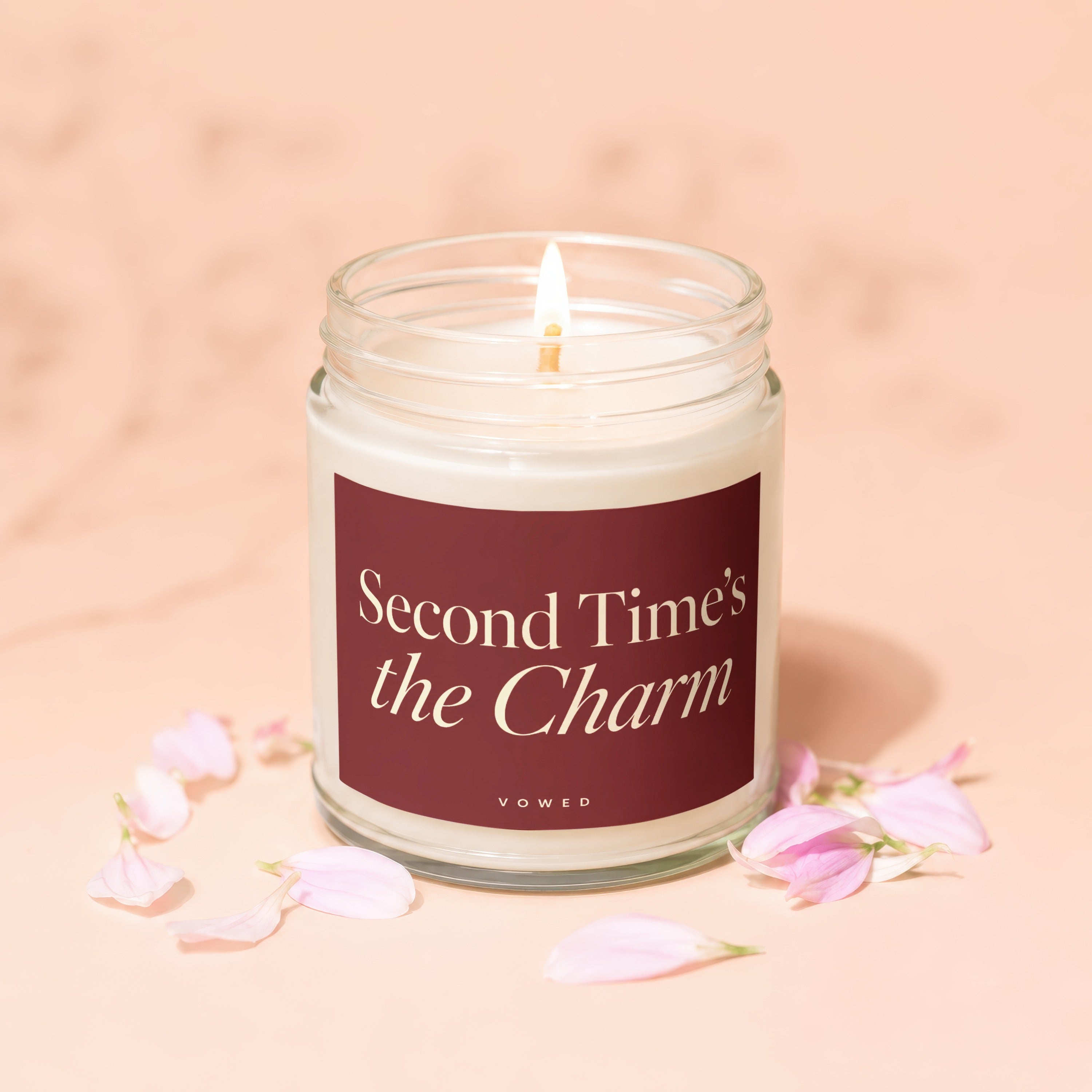 Glass candle with lit wick, text "Second Time's the Charm" and "VOWED".