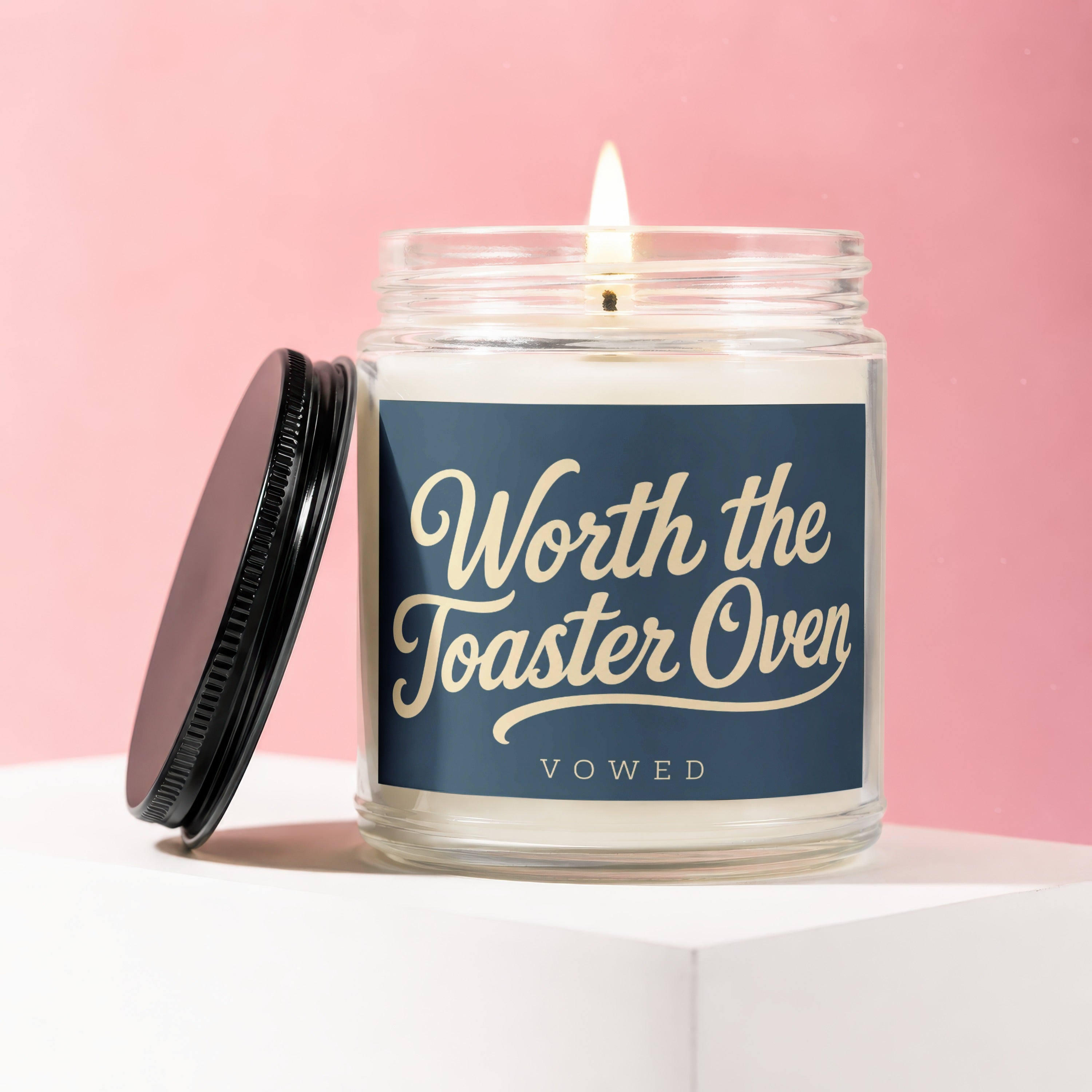 Glass jar candle with lit wick, "Worth the Toaster Oven" text on label.