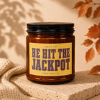 Amber candle with black lid displays a yellow label reading "HE HIT THE JACKPOT" by Vowed Candle Co.