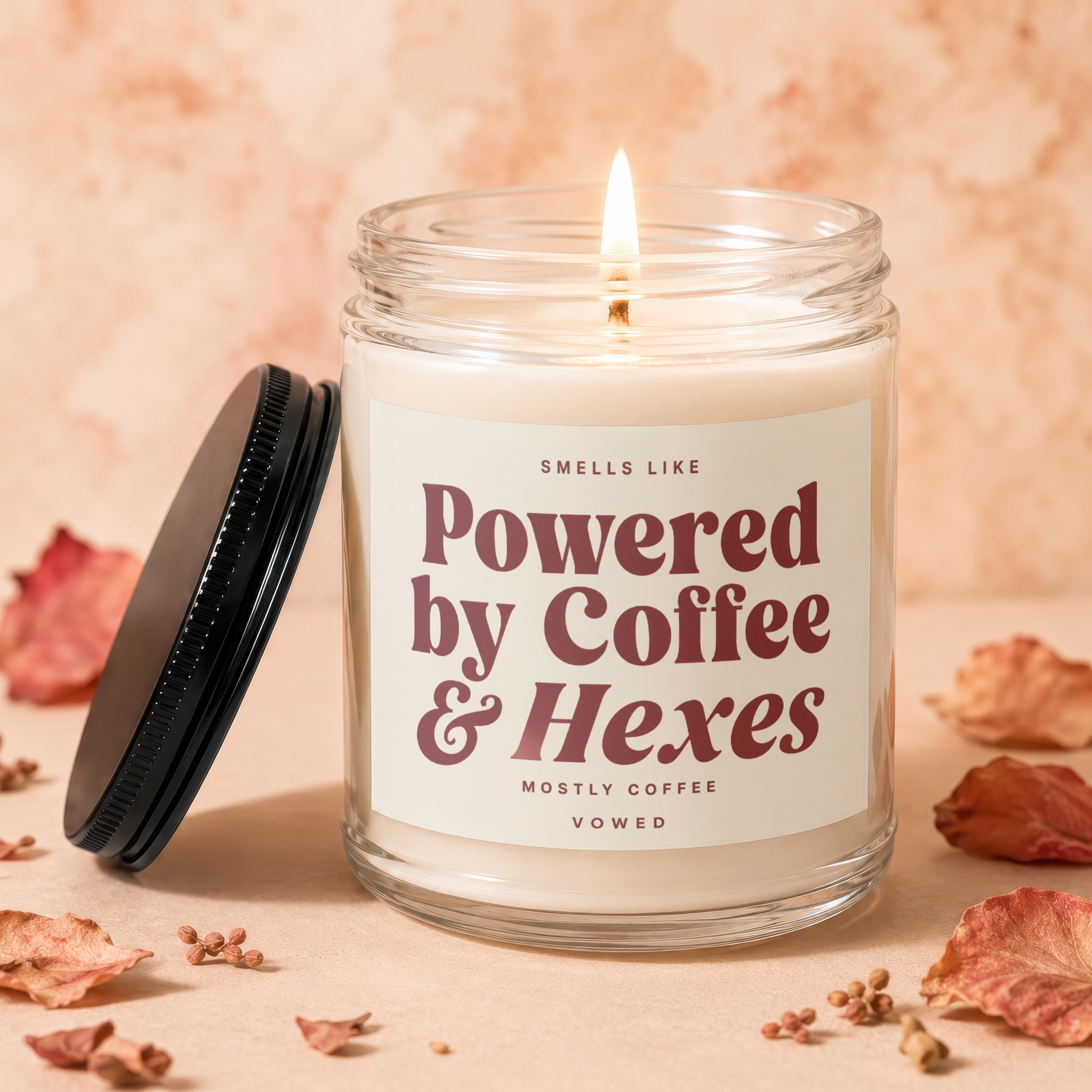 Lit candle in glass jar with label "Smells like Powered by Coffee & Hexes".