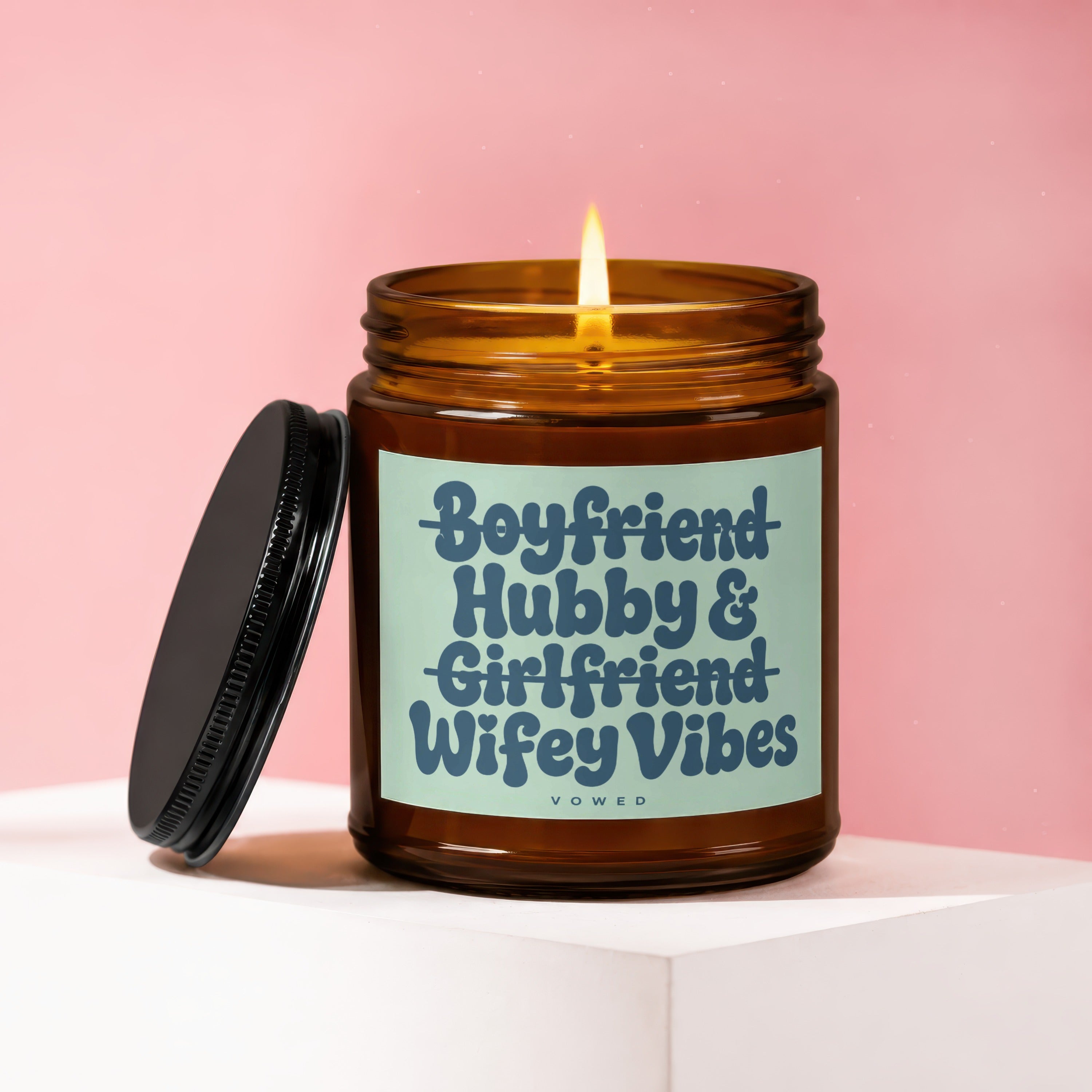 A lit candle in amber glass jar with "Boyfriend Hubby & Girlfriend Wifey Vibes" text.