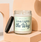 Glass candle with black lid, reads "Smells Like Love Lights the Way".