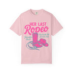 Pink t-shirt with "Her Last Rodeo" graphic, cowboy boots, and hat.