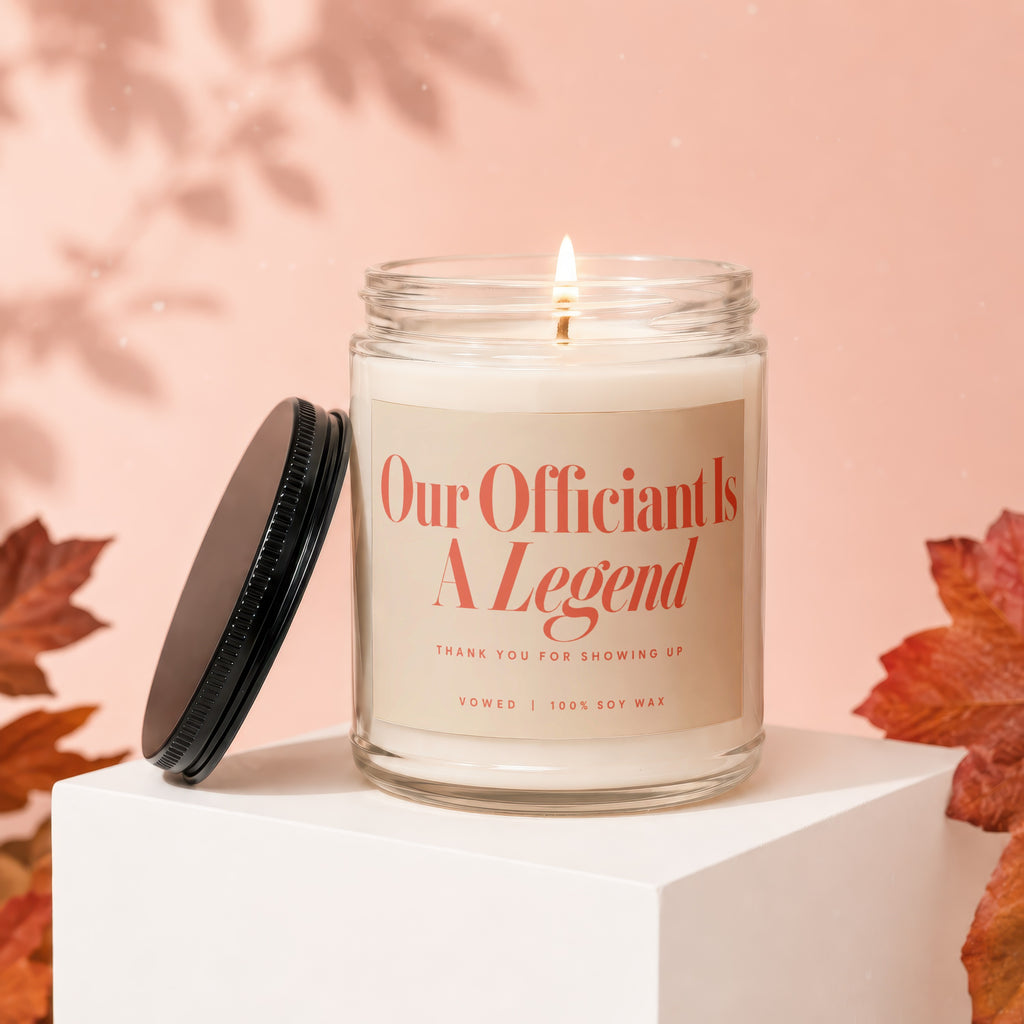 Glass candle with lit wick features label "Our Officiant Is A Legend."