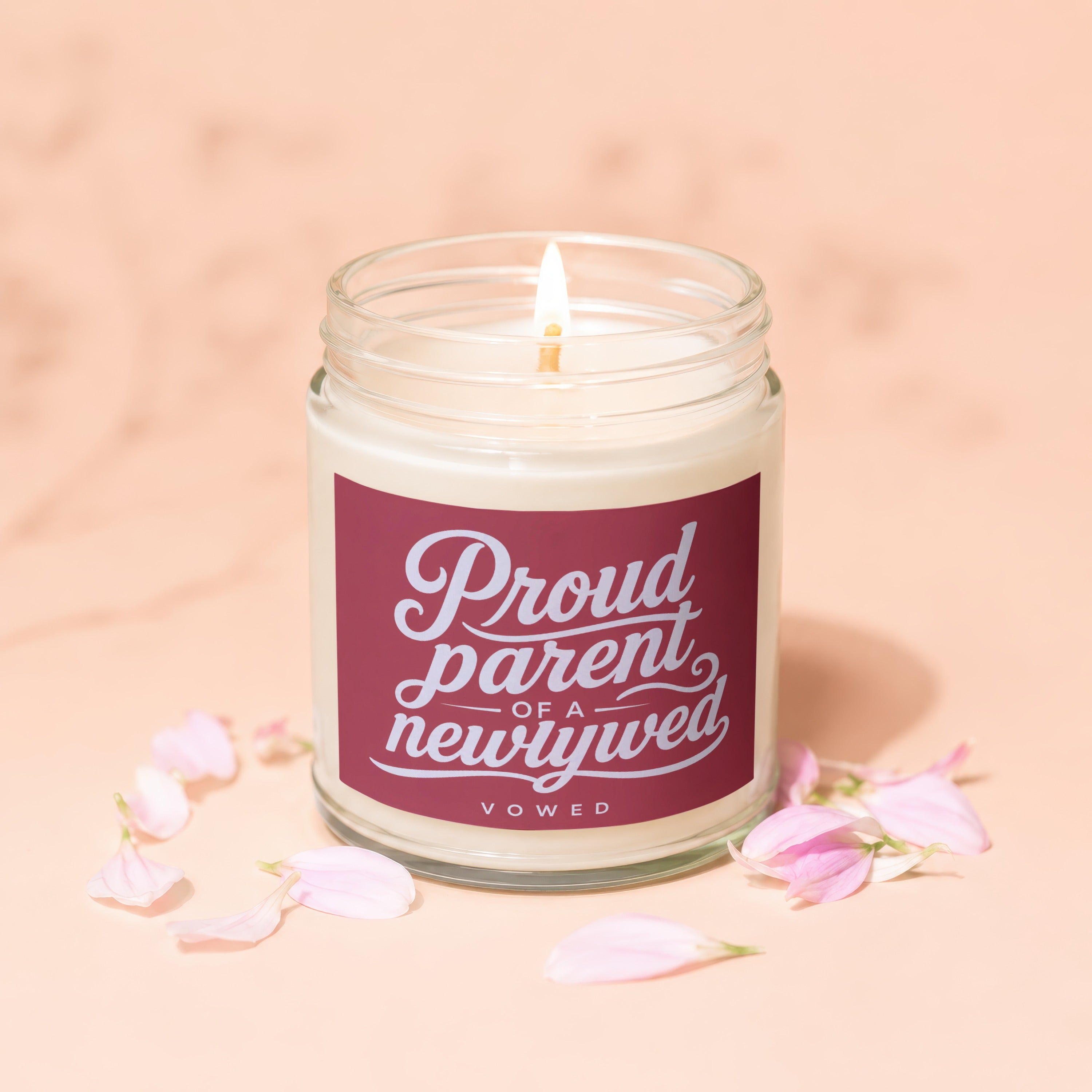 Lit candle in glass jar with "Proud parent of a newlywed, vowed" text surrounded by flower petals.