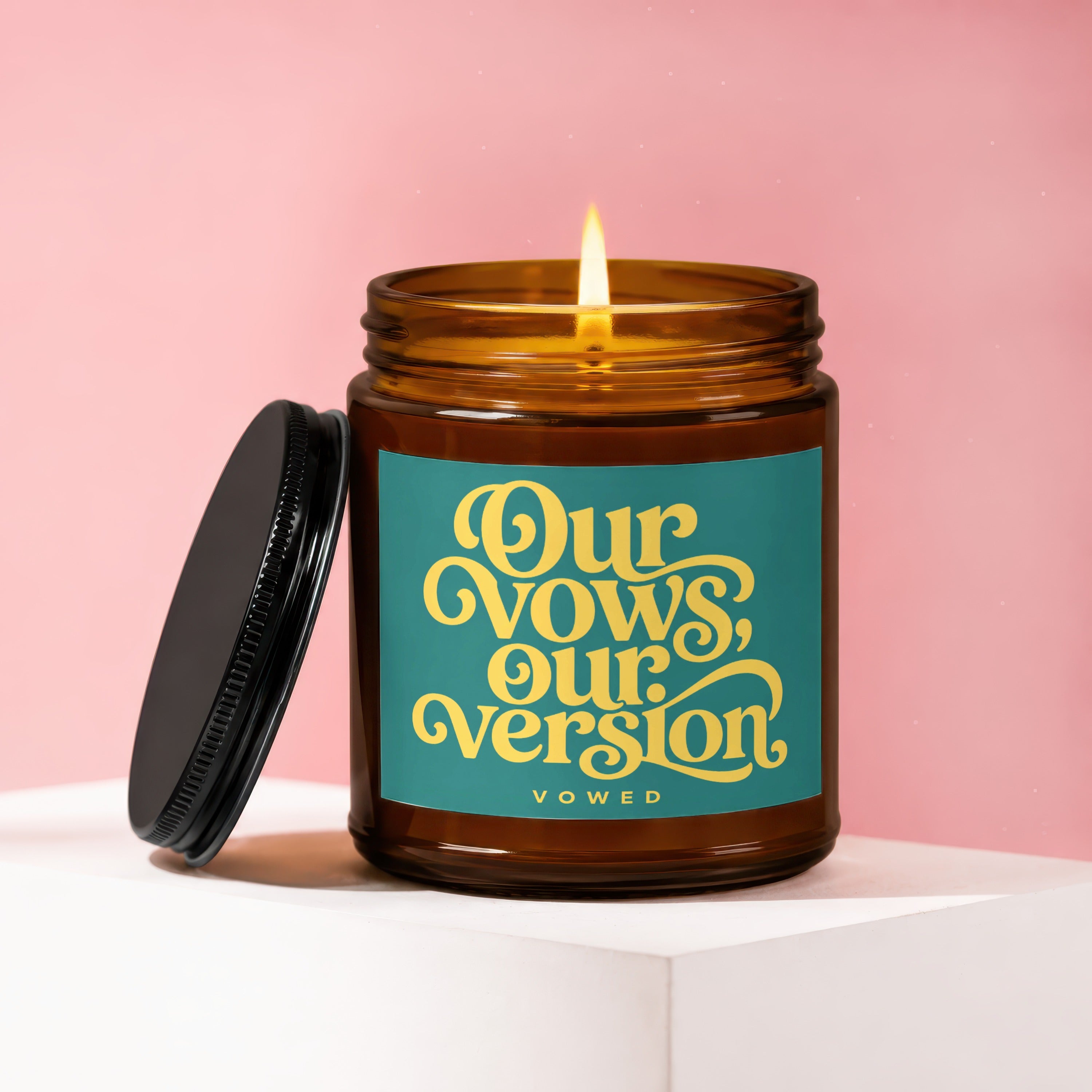 Amber candle with burning wick and black lid, featuring text "Our Vows, Our Version".
