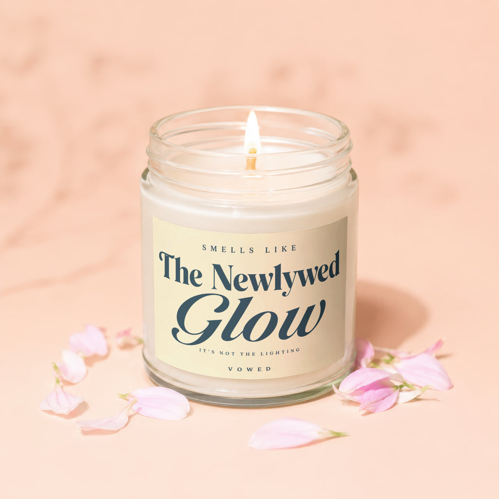 Lit candle with "The Newlywed Glow" label surrounded by pink petals.