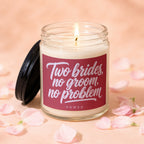 Glass jar candle with lit wick and pink petals, reads "Two brides, no groom, no problem."