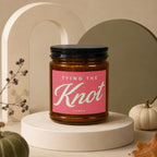 Amber candle with pink label that reads "Tying the Knot" and "Vowed".