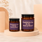 Two amber glass candles with purple labels reading "Thankful for You. Be My Maid of Honor?"
