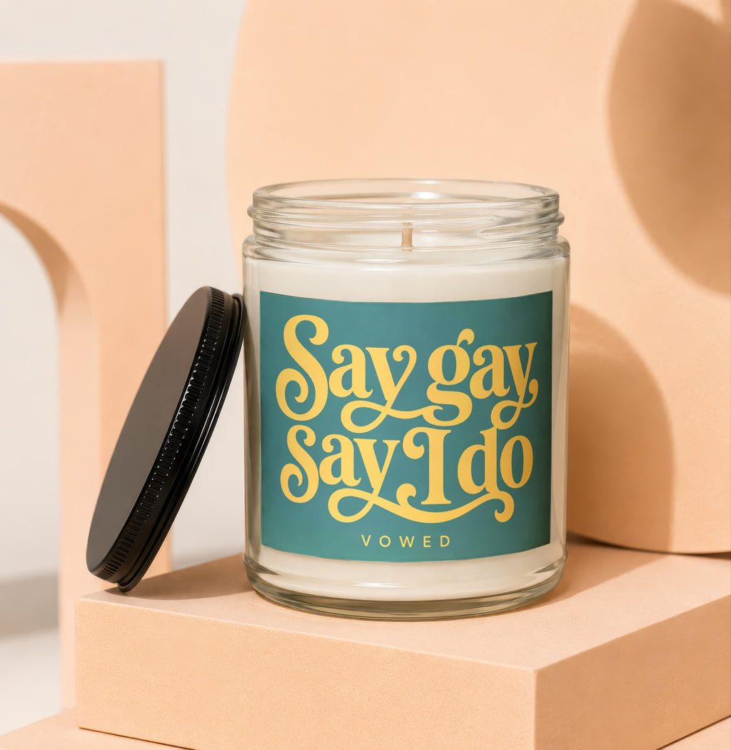 Glass candle with "Say gay Say I do" text in yellow on teal label.
