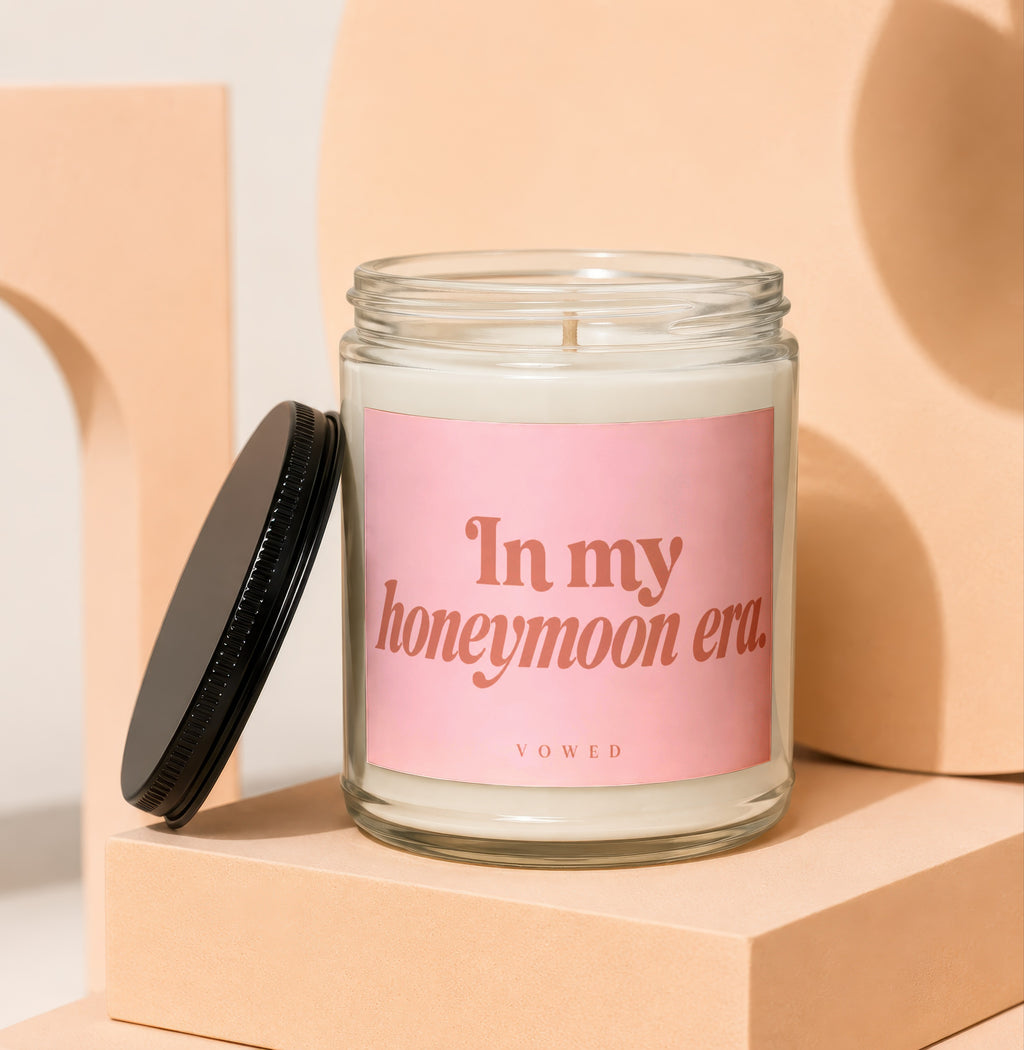 Glass candle with pink label reading "In my honeymoon era. VOWED."