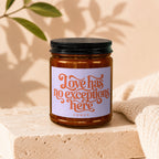 Amber glass candle with a black lid, featuring a lavender label with "Love has no exceptions here" text.