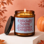 Candle with text "Officially Losing, Gaining a Daughter" on label.