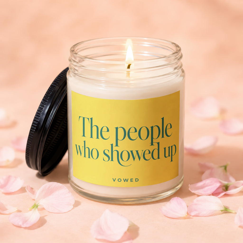 Jar candle with lit wick and a yellow label reading "The people who showed up VOWED".