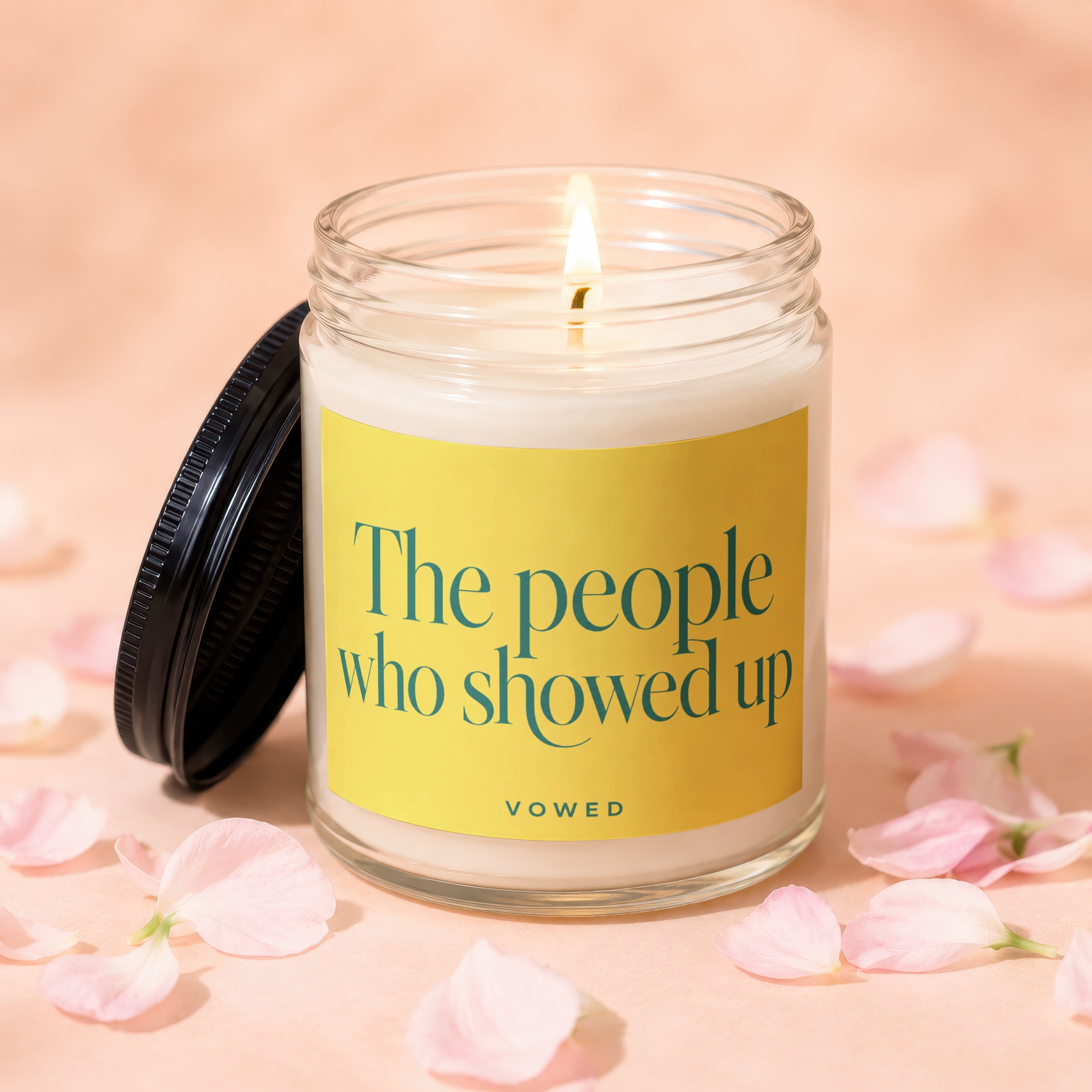 Jar candle with lit wick and a yellow label reading "The people who showed up VOWED".