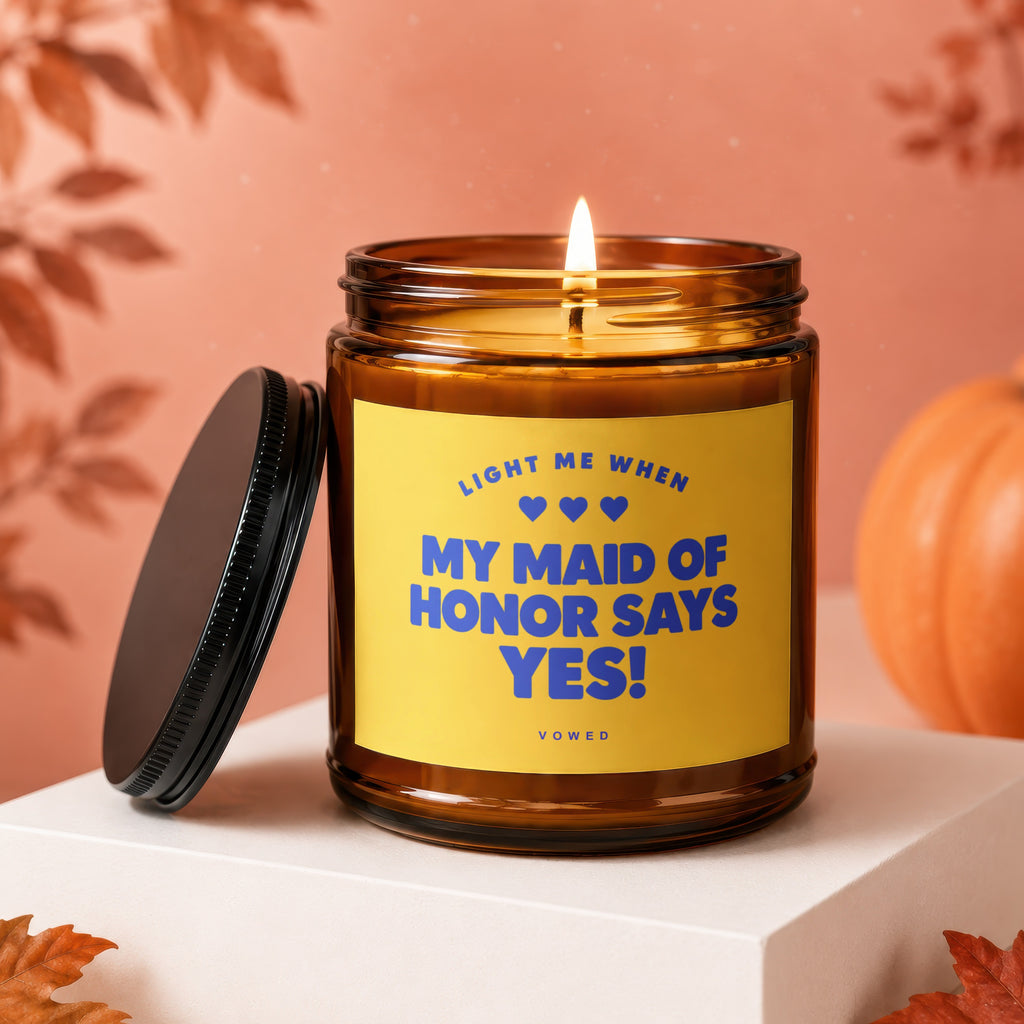 Amber jar candle with yellow label reading "LIGHT ME WHEN MY MAID OF HONOR SAYS YES!".