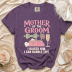Purple t-shirt with "Mother of the Groom" text, clutch, and accessories.